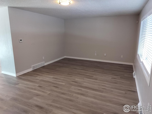 unfurnished room featuring visible vents, a textured ceiling, baseboards, and wood finished floors