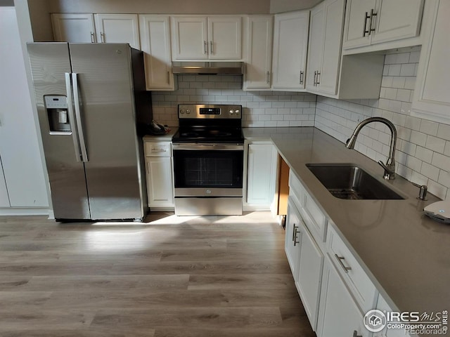 kitchen featuring white cabinets, light wood-style floors, stainless steel appliances, under cabinet range hood, and a sink