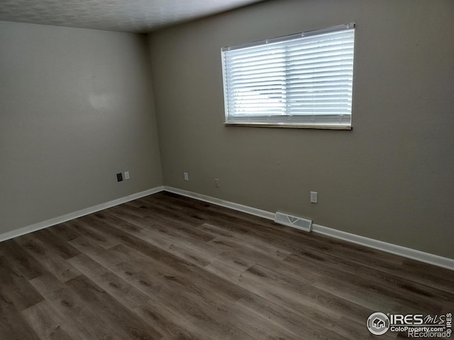 empty room with visible vents, dark wood finished floors, and baseboards