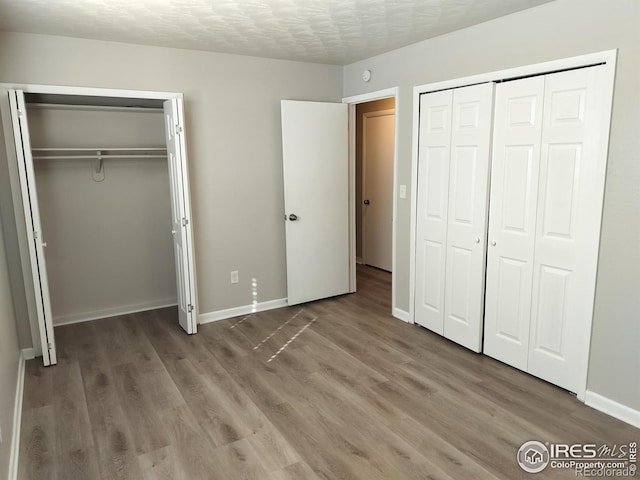 unfurnished bedroom with a textured ceiling, baseboards, and wood finished floors