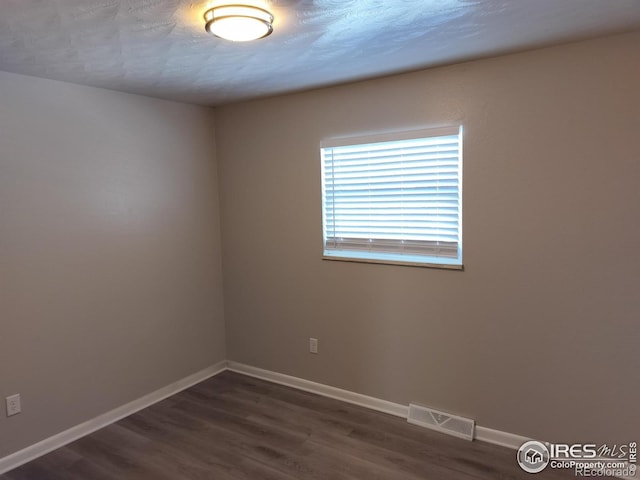 empty room featuring baseboards, a textured ceiling, visible vents, and dark wood-style flooring