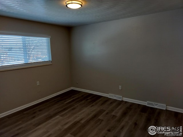 spare room featuring dark wood-style flooring, visible vents, and baseboards