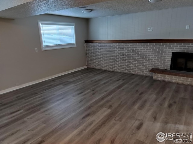 basement featuring a brick fireplace, a textured ceiling, baseboards, and wood finished floors