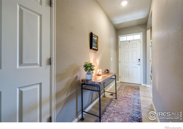 doorway to outside with light wood-style flooring, baseboards, and a textured wall