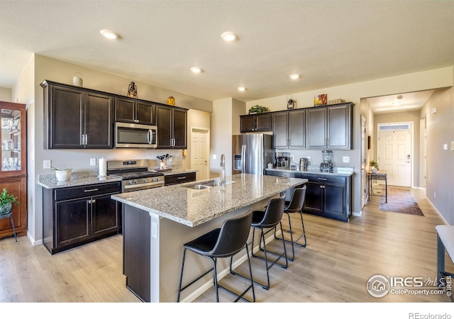 kitchen featuring a sink, a kitchen breakfast bar, appliances with stainless steel finishes, light stone countertops, and an island with sink