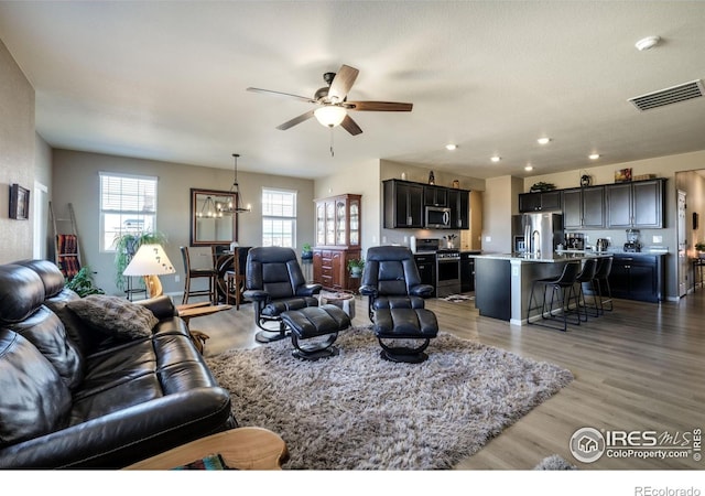 living room featuring ceiling fan with notable chandelier, light wood finished floors, visible vents, and recessed lighting