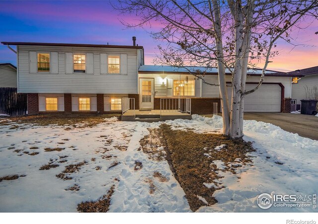 split level home featuring driveway, an attached garage, a porch, and brick siding