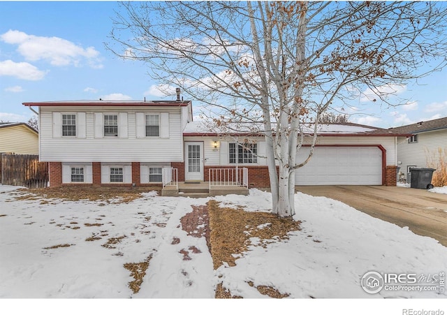 split level home with concrete driveway, brick siding, an attached garage, and fence