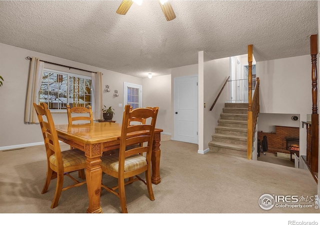 dining room with a fireplace, stairway, a ceiling fan, light carpet, and a textured ceiling