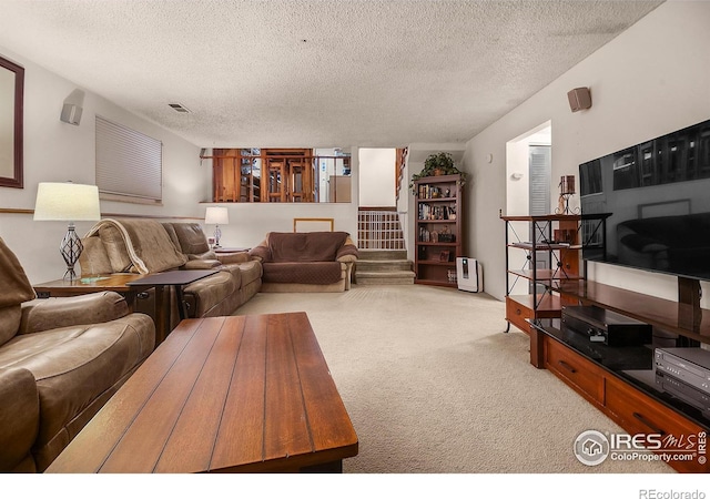 living room featuring light carpet, stairs, visible vents, and a textured ceiling