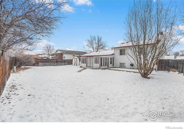 snow covered property featuring an outbuilding, a fenced backyard, and a storage unit