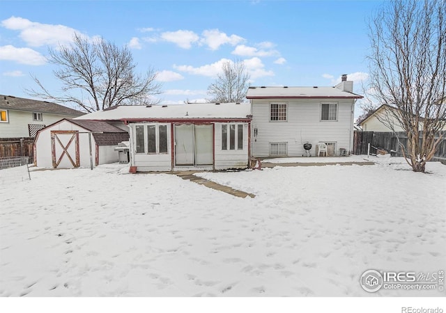 snow covered back of property with a garage, fence, a chimney, and a shed