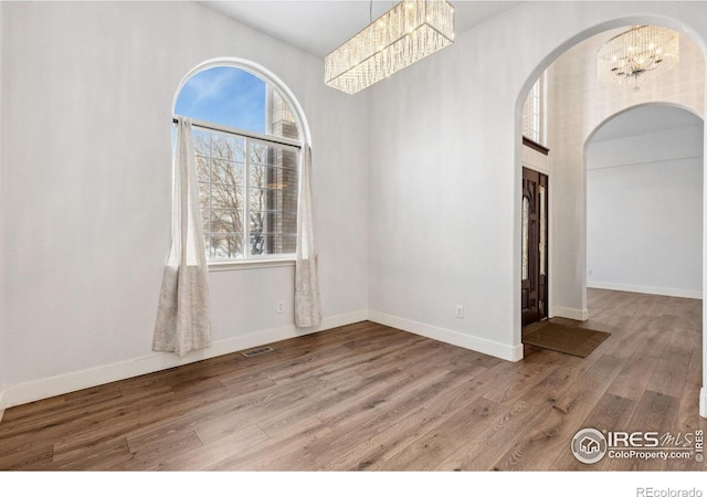 empty room with arched walkways, visible vents, a healthy amount of sunlight, wood finished floors, and a chandelier