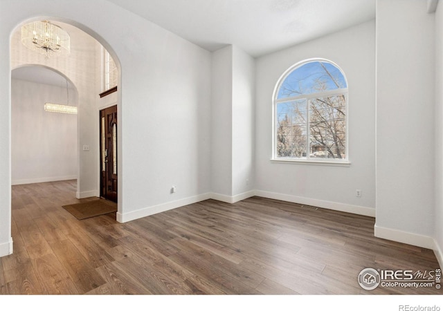 spare room featuring arched walkways, wood finished floors, and baseboards