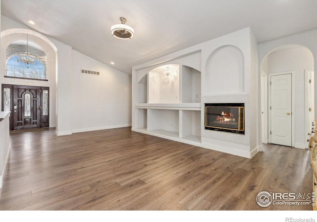 unfurnished living room featuring built in shelves, a notable chandelier, lofted ceiling, visible vents, and wood finished floors