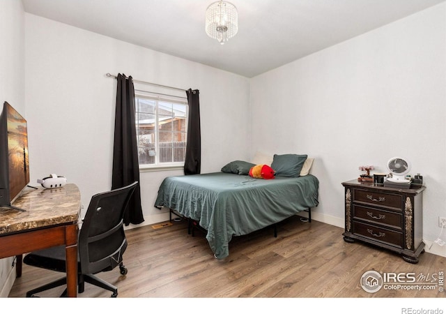 bedroom with an inviting chandelier, light wood-style flooring, and baseboards