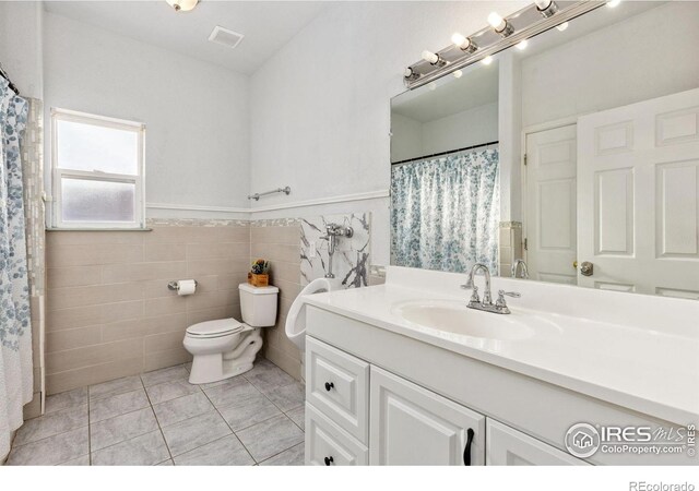 bathroom with visible vents, wainscoting, toilet, vanity, and tile walls