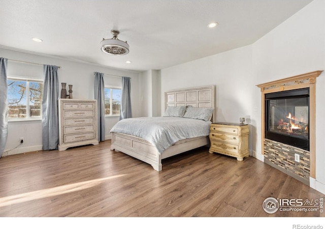 bedroom featuring a glass covered fireplace, recessed lighting, baseboards, and wood finished floors