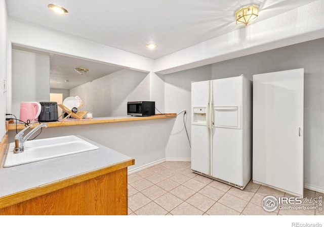 kitchen with light tile patterned floors, light countertops, a sink, white fridge with ice dispenser, and baseboards