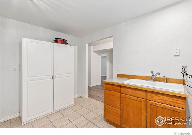 kitchen featuring light tile patterned floors, light countertops, brown cabinetry, a sink, and baseboards