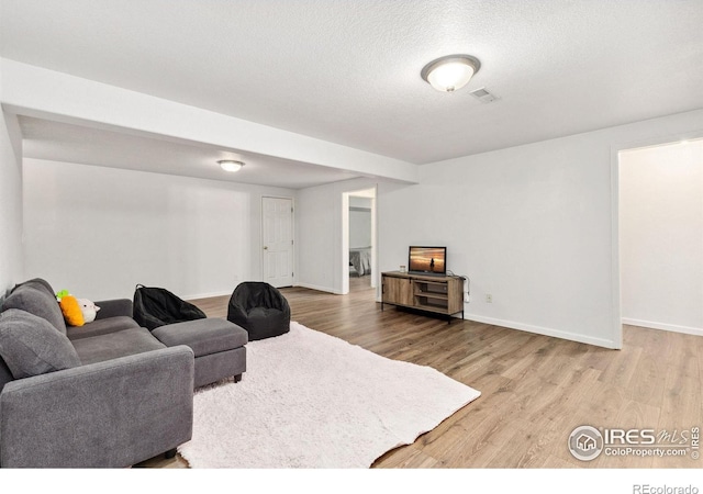 living room with baseboards, a textured ceiling, visible vents, and wood finished floors