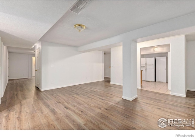 finished basement featuring white fridge with ice dispenser, visible vents, baseboards, and wood finished floors