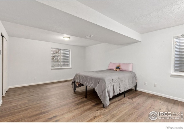 bedroom with baseboards, a textured ceiling, visible vents, and wood finished floors