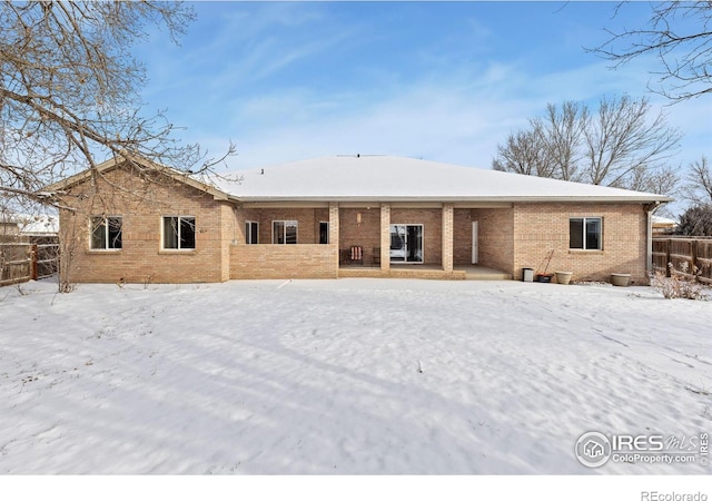 snow covered rear of property featuring brick siding and fence