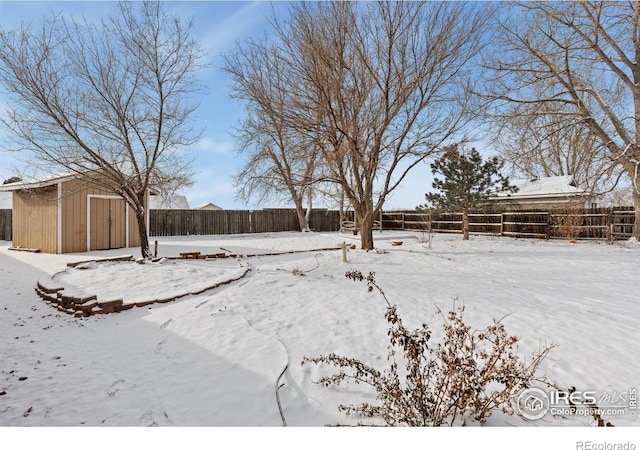 yard layered in snow featuring a storage unit, an outdoor structure, and fence