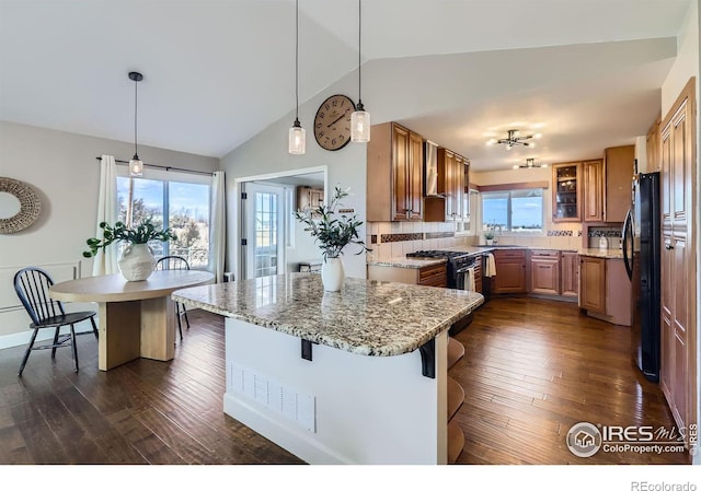 kitchen featuring a breakfast bar, pendant lighting, brown cabinetry, freestanding refrigerator, and light stone countertops