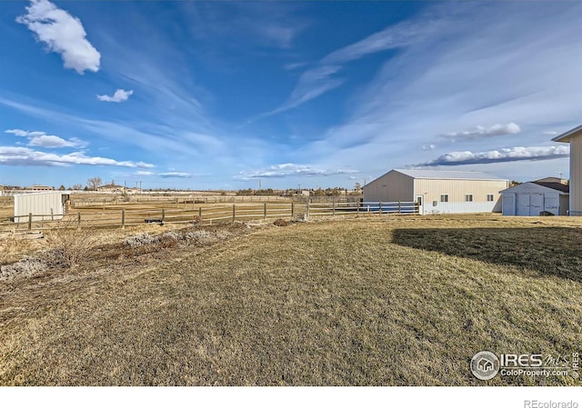 view of yard featuring an outbuilding, a rural view, an outdoor structure, and fence