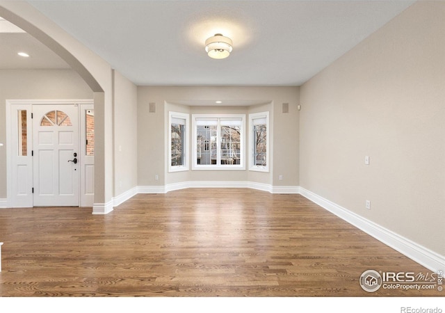 foyer with arched walkways, recessed lighting, wood finished floors, and baseboards