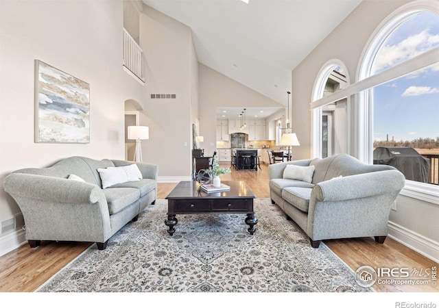 living room featuring high vaulted ceiling, baseboards, visible vents, and wood finished floors