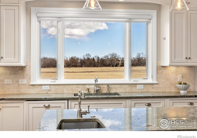 kitchen featuring stone counters, a sink, white cabinetry, and decorative backsplash