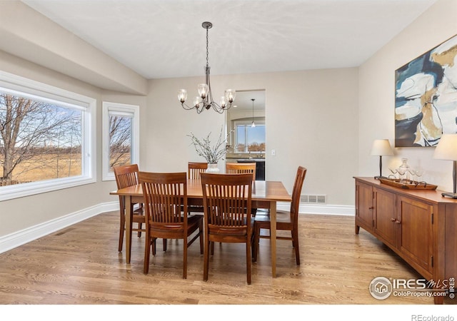 dining room featuring light wood-type flooring, visible vents, baseboards, and an inviting chandelier