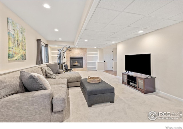 living room featuring built in features, recessed lighting, a tiled fireplace, light carpet, and baseboards