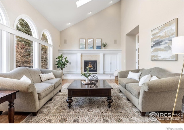 living area with a skylight, high vaulted ceiling, wood finished floors, and a tile fireplace