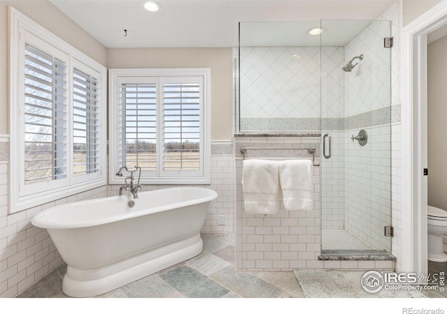 bathroom with recessed lighting, tile walls, a freestanding bath, wainscoting, and a stall shower