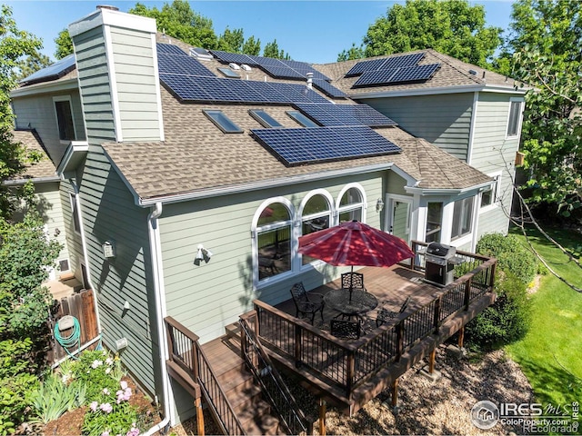 rear view of house with solar panels, a shingled roof, outdoor dining area, and a wooden deck