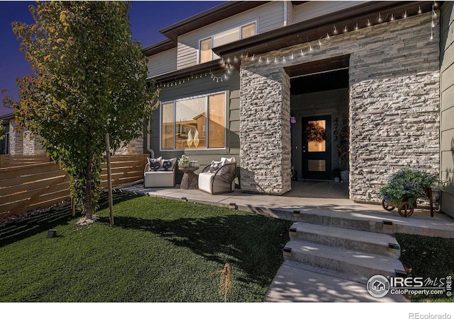 property entrance featuring stone siding, a lawn, and a patio