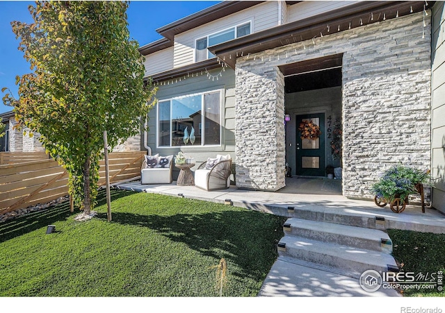 entrance to property featuring stone siding, a yard, fence, and a patio