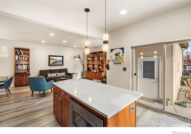 kitchen with light countertops, light wood-type flooring, a center island, stainless steel microwave, and decorative light fixtures