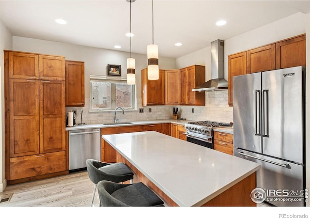 kitchen featuring a sink, wall chimney range hood, high end appliances, and light countertops