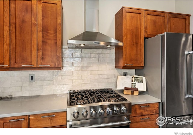 kitchen featuring stainless steel appliances, light countertops, decorative backsplash, brown cabinetry, and wall chimney range hood