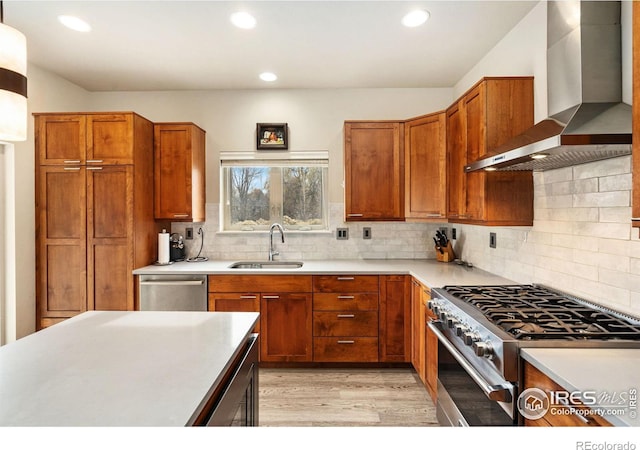 kitchen with light wood finished floors, light countertops, appliances with stainless steel finishes, a sink, and wall chimney exhaust hood