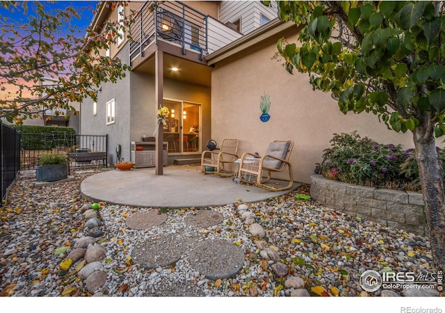 rear view of house with a balcony, a patio area, fence, and stucco siding