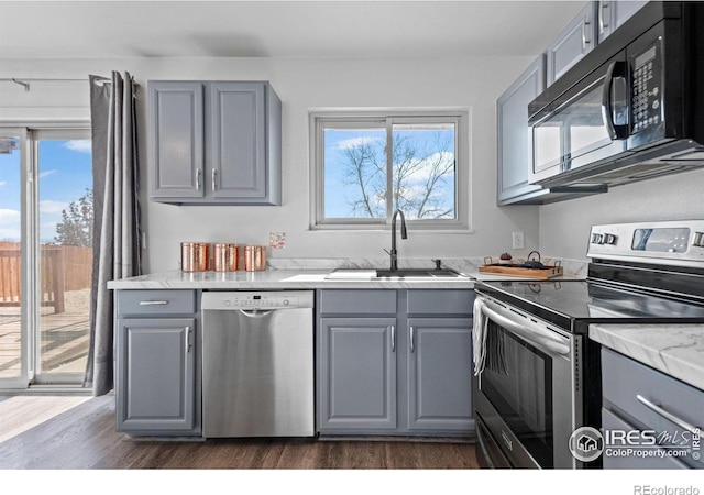 kitchen with light stone counters, appliances with stainless steel finishes, dark wood-style flooring, gray cabinets, and a sink