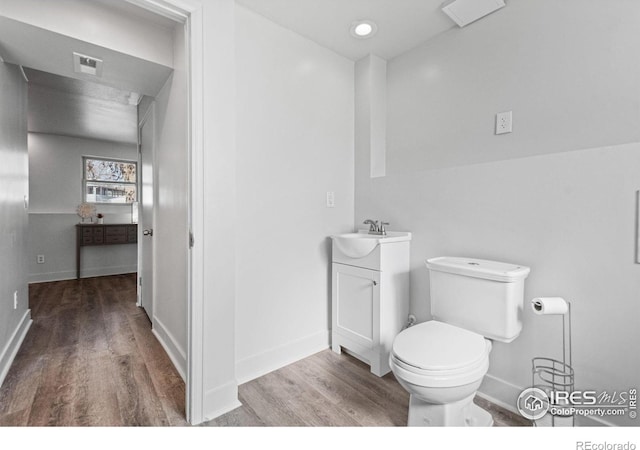 half bathroom featuring visible vents, toilet, vanity, wood finished floors, and baseboards