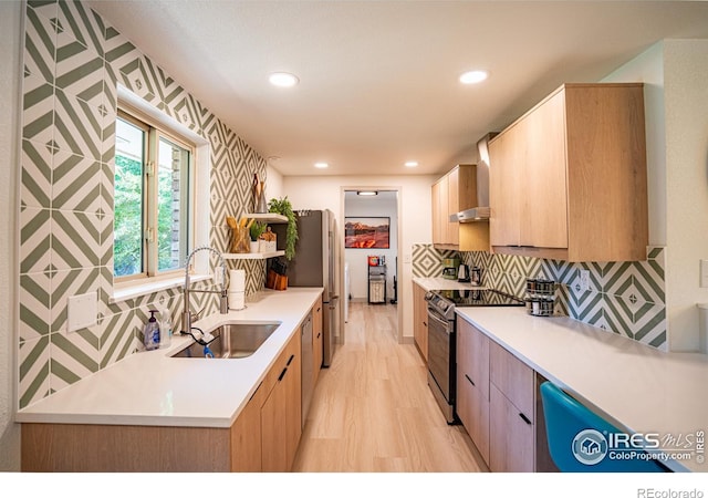 kitchen featuring appliances with stainless steel finishes, light countertops, a sink, and wall chimney exhaust hood