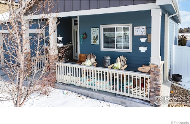 snow covered property entrance featuring covered porch and board and batten siding